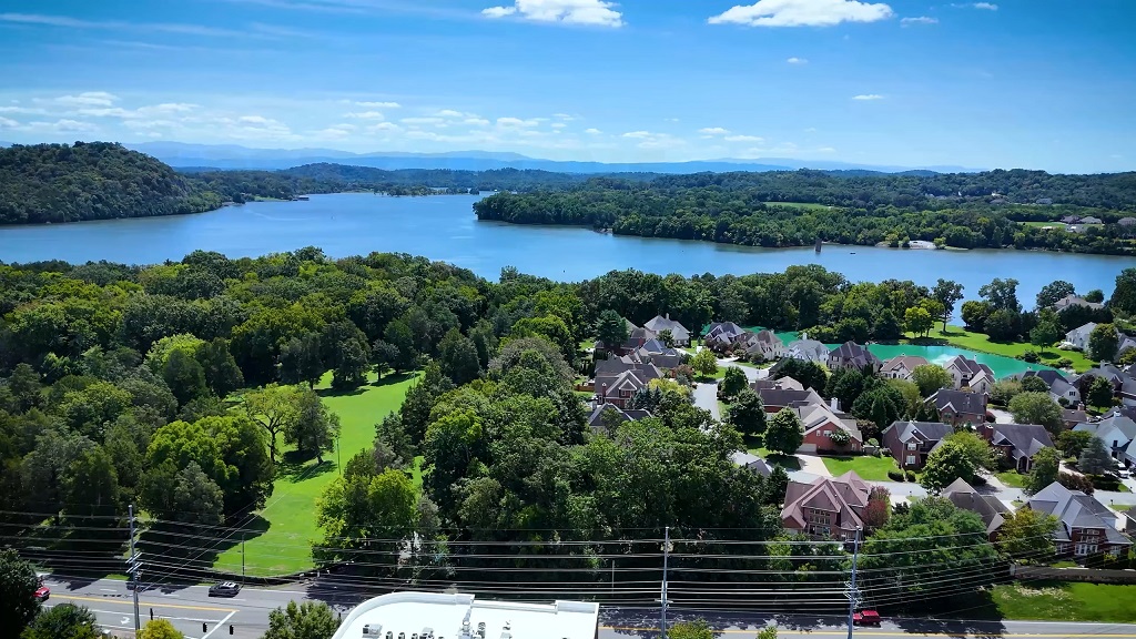 Aerial view of a peaceful suburban neighborhood surrounded by lush greenery and a large lake in Tennessee under a clear blue sky