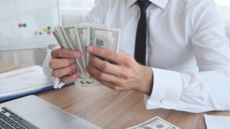 A man in a white shirt and tie counting cash at his desk, illustrating the average salary in the US