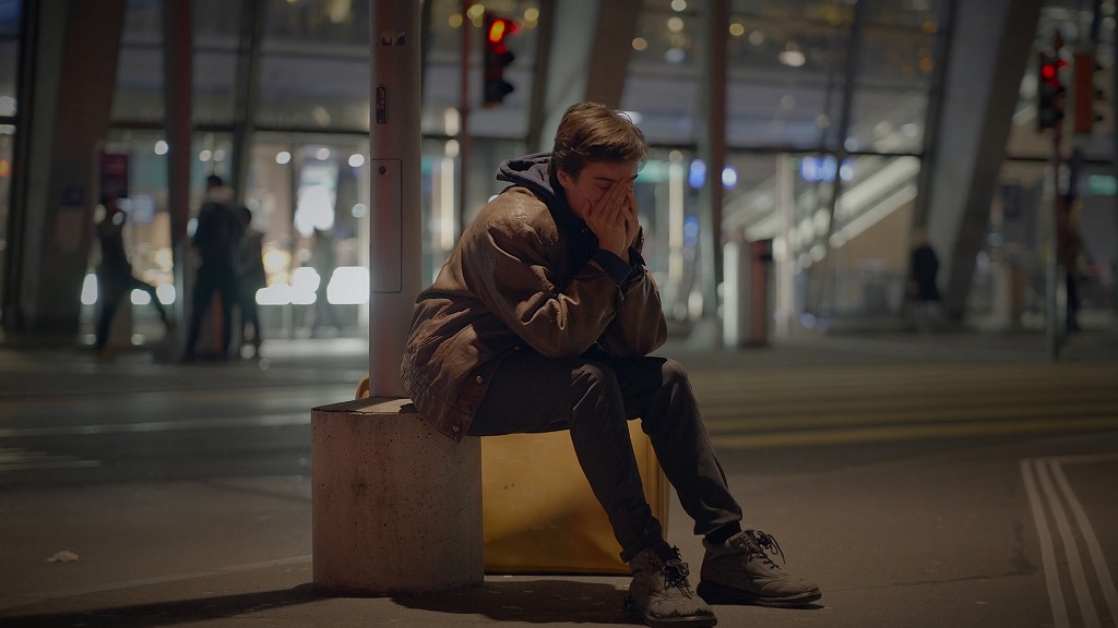 Homeless immigrant man sitting alone at night, reflecting mental health struggles