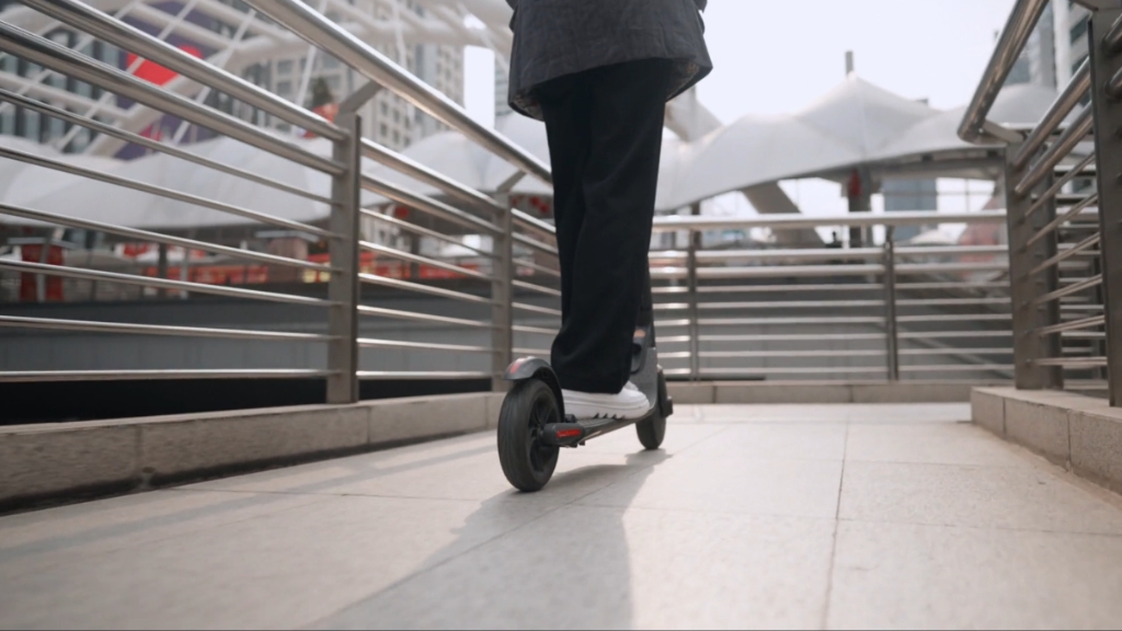 A person rides an electric scooter across a city bridge, showing how teens and adults drive an e-scooter in urban areas