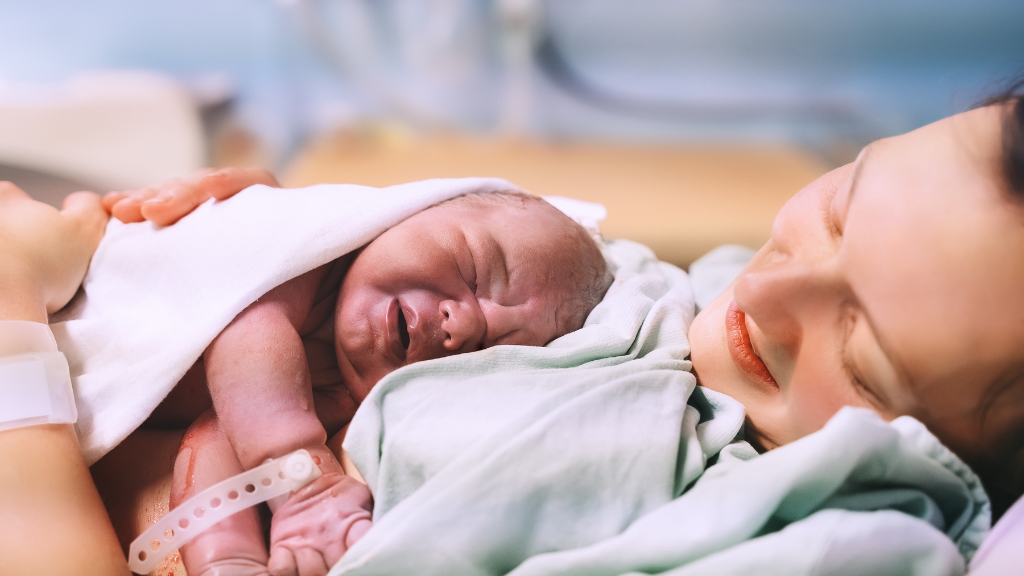 A newborn baby rests on the mother’s chest right after birth, both wrapped in hospital blankets
