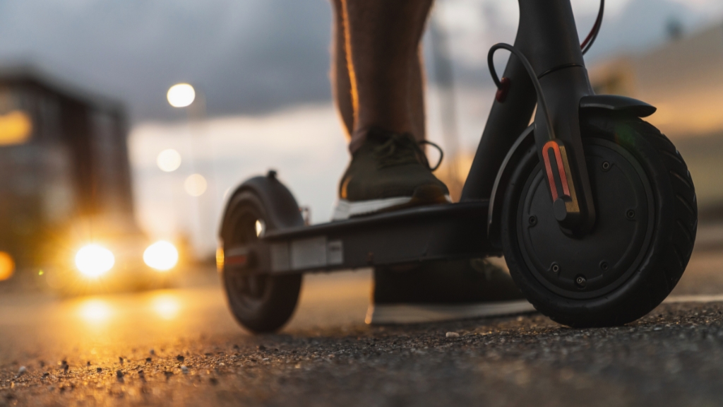 A person rides an electric scooter on a city street at dusk