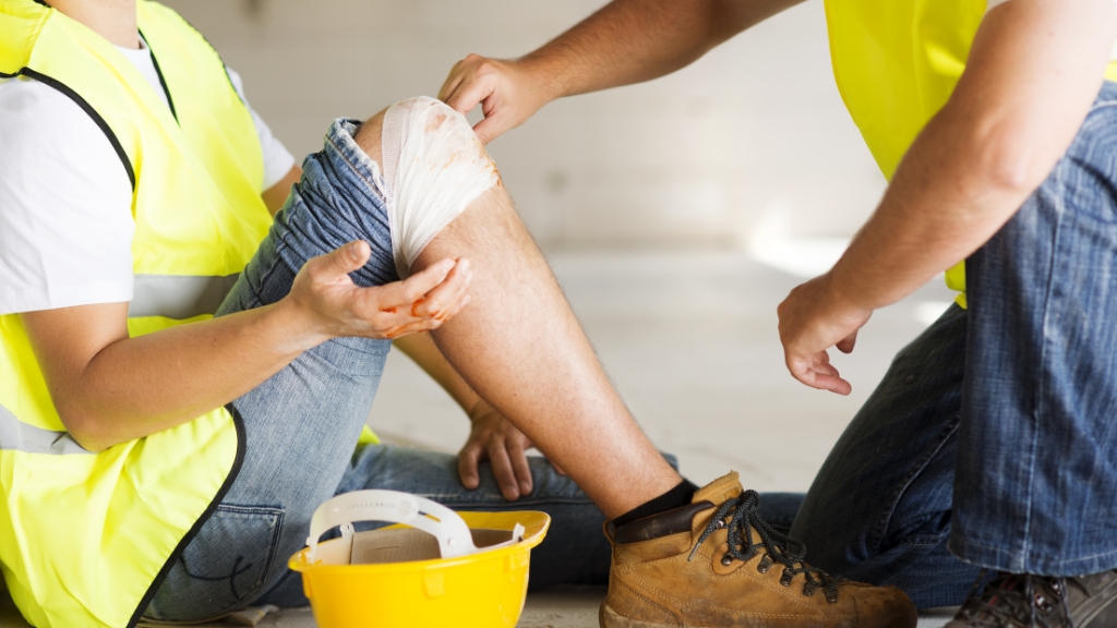 Two workers in safety vests treat a knee injury at a construction site, showing the real meaning of accident vs incident