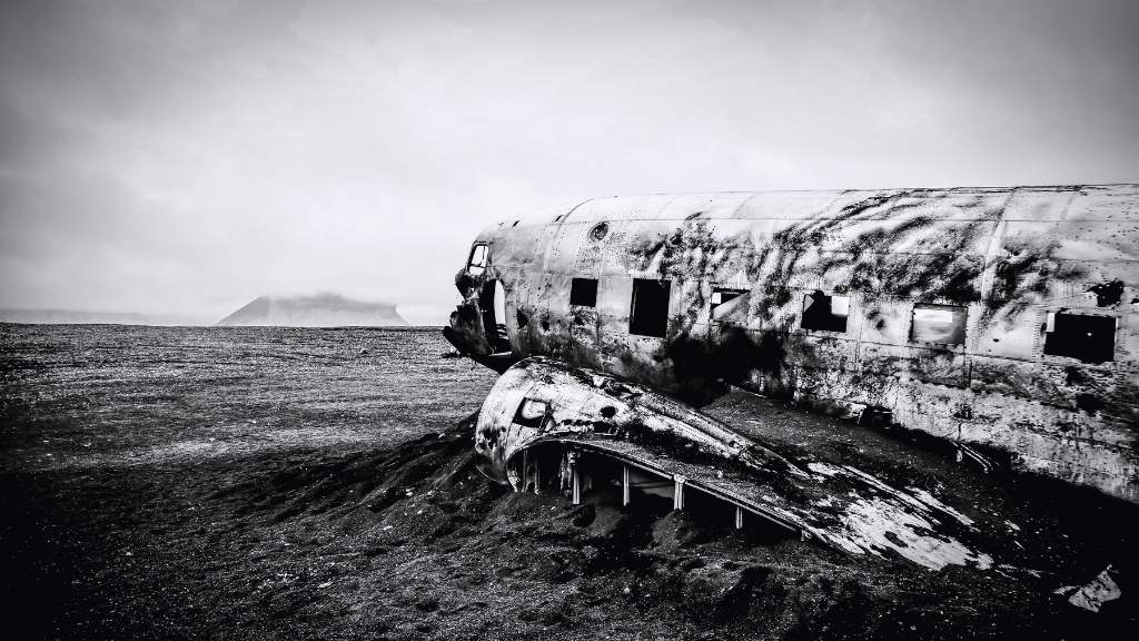A black and white photo of a burned airplane wreck resting on an empty field
