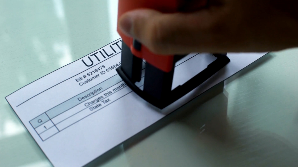 A hand stamps a utility bill, symbolizing average monthly utility costs in the US