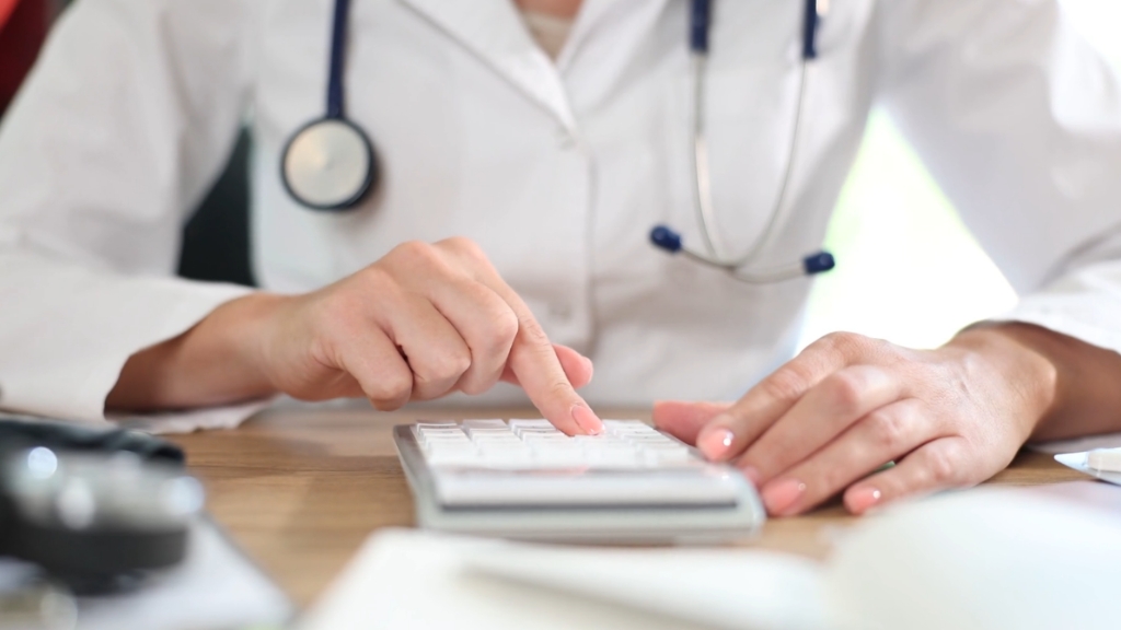 A doctor using a calculator to review healthcare costs at a desk