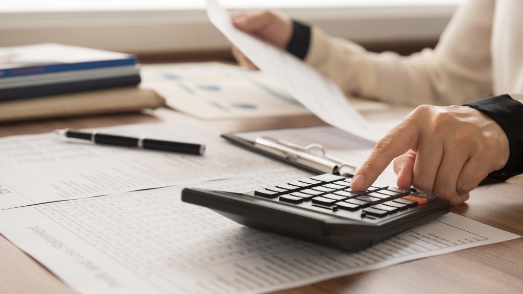 A person reviews documents and uses a calculator while planning expenses before relocating to the US for work