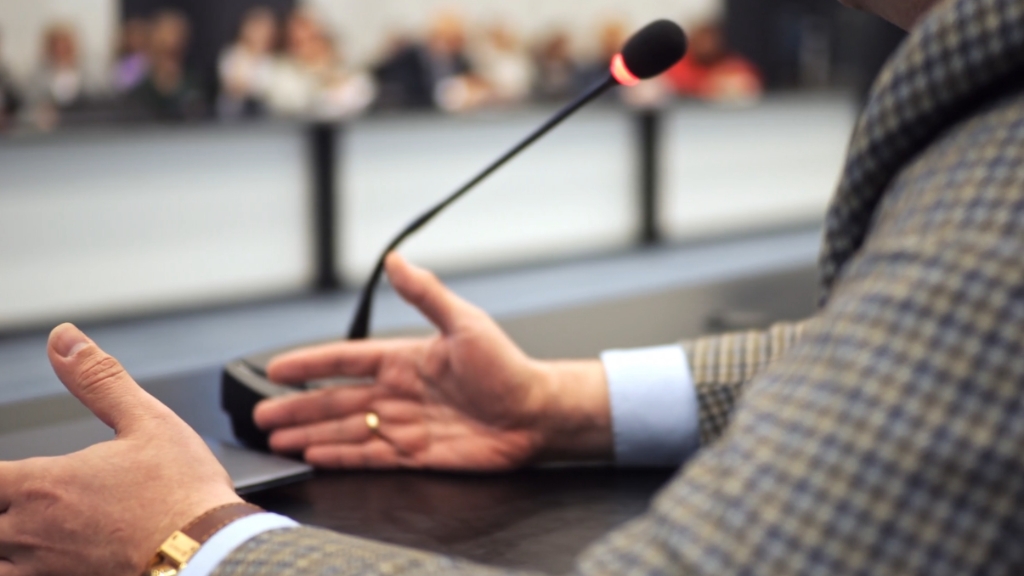 A man speaks into a microphone at a meeting, symbolizing political discussions driven by Florida’s rapid population growth