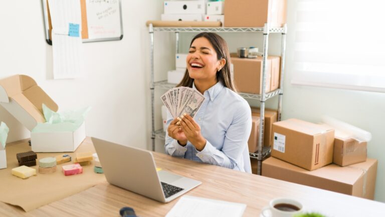 A young woman smiles at her desk with cash and packages, showing income opportunities through digital platforms