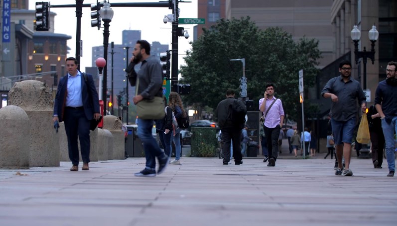 People walking on a city sidewalk with buildings and traffic lights in the background