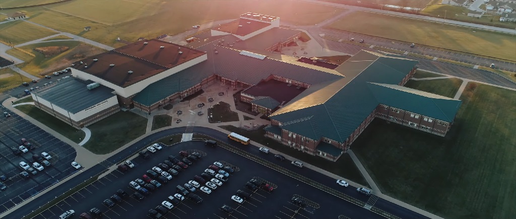 Aerial view of Perrysburg High School in Ohio at sunset, showing the large school complex with green roofs, parking lots, and surrounding open fields