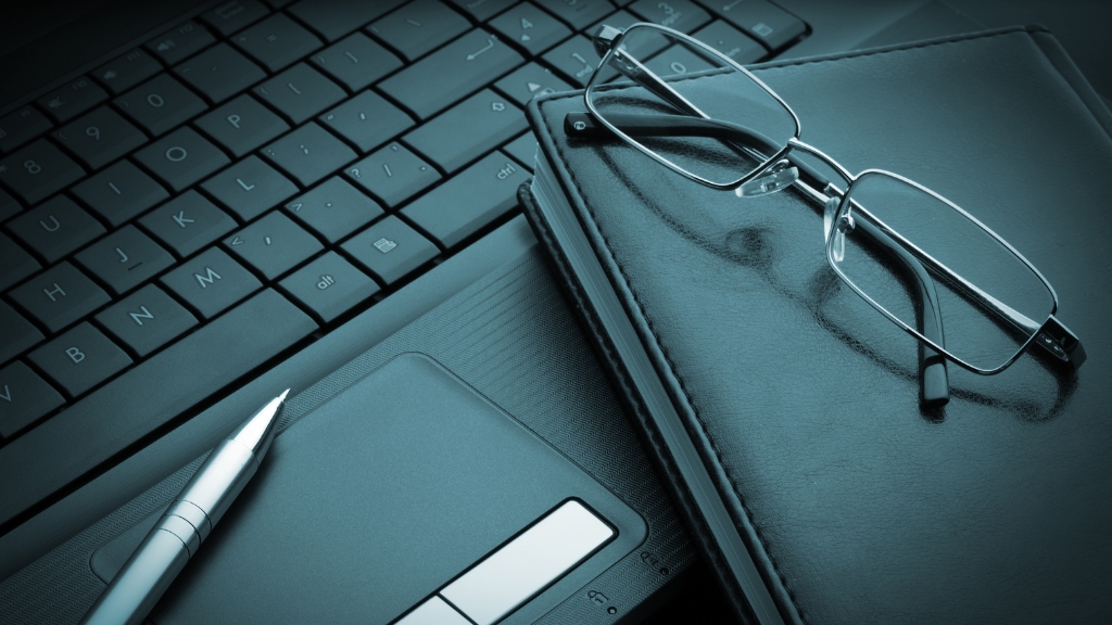 A laptop with a pen, notebook, and glasses on top illustrates some of the cheapest promo items for small businesses