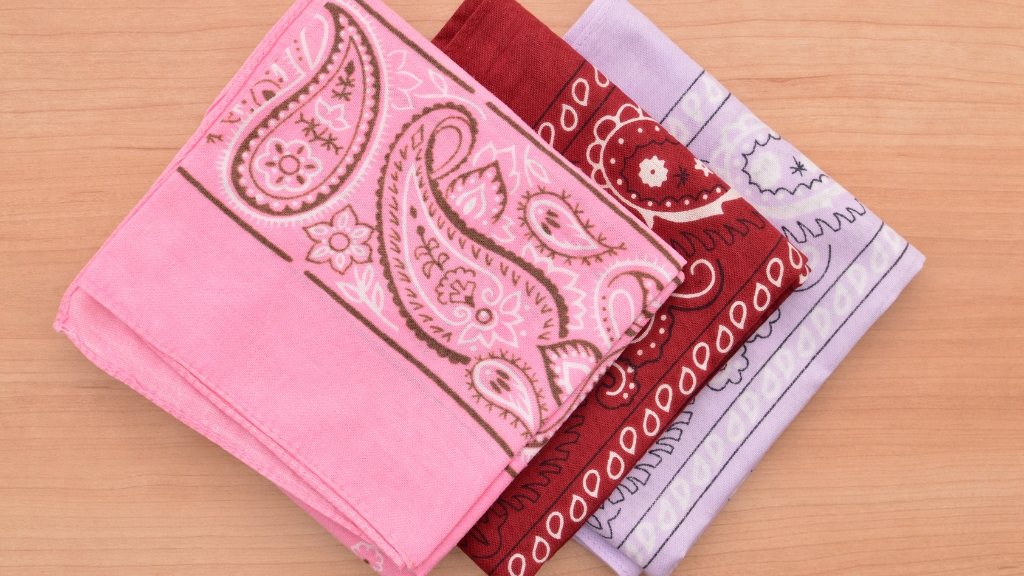 Three folded bandanas in pink, red, and lavender with paisley patterns laid on a wooden surface