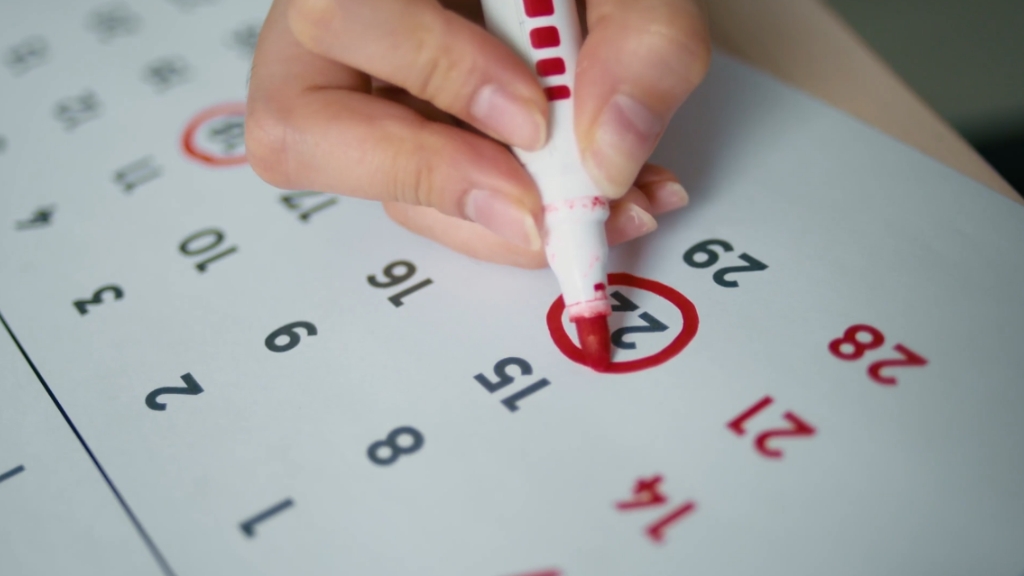 A hand uses a red marker to circle a date on a paper calendar