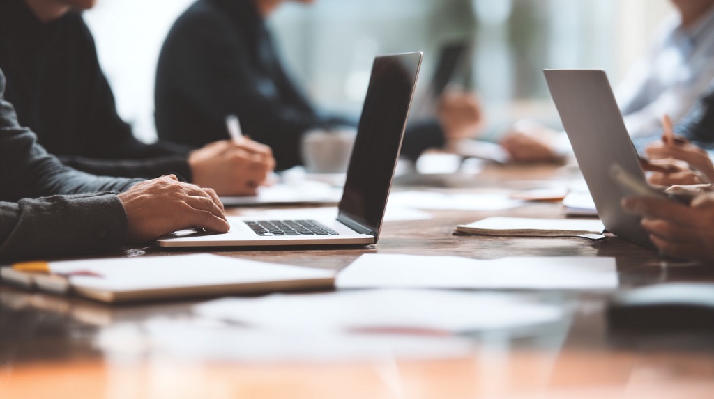 Group of professionals working on laptops during a meeting, focusing on business data