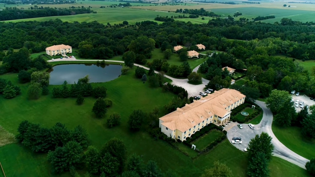 Aerial view of Maharishi Vedic City showing yellow buildings surrounded by trees, open fields, and a pond, illustrating its peaceful and eco-friendly layout