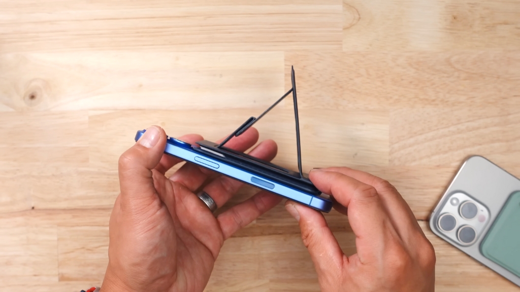 Hands hold a blue smartphone with a built-in stand propped open on a wooden surface
