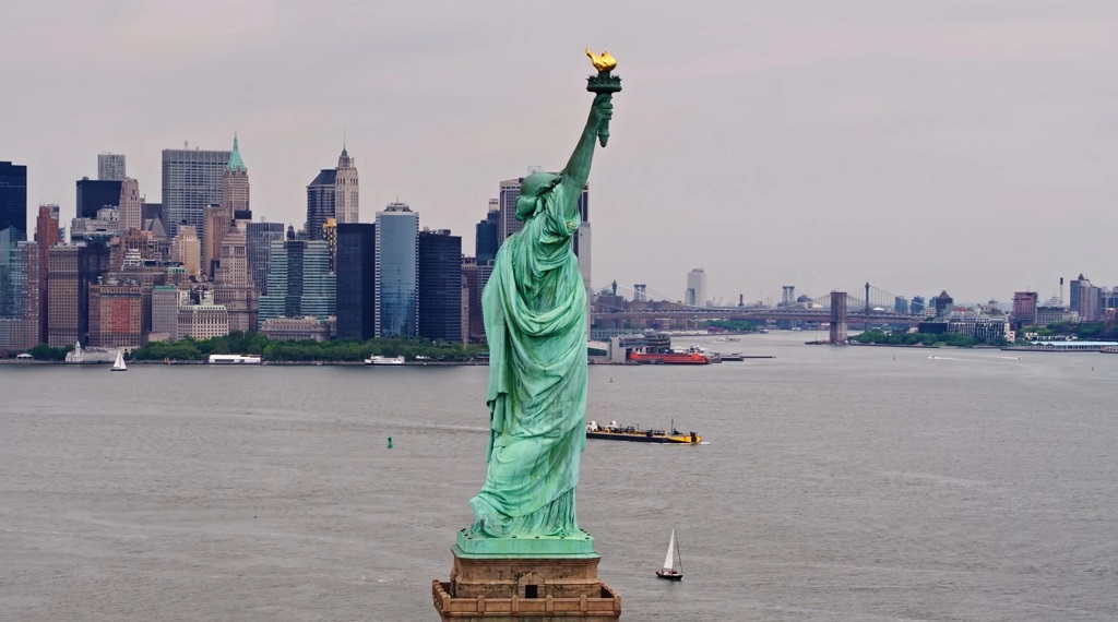Statue of Liberty facing Manhattan skyline across the Hudson River on a cloudy day