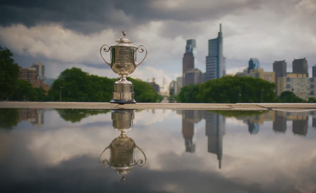 Silver golf championship trophy displayed outdoors with the Philadelphia skyline reflected in a glossy surface beneath it