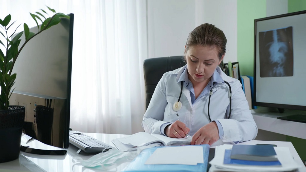 Female doctor sitting at her desk, reviewing medical documents and patient records in a clinical office environment