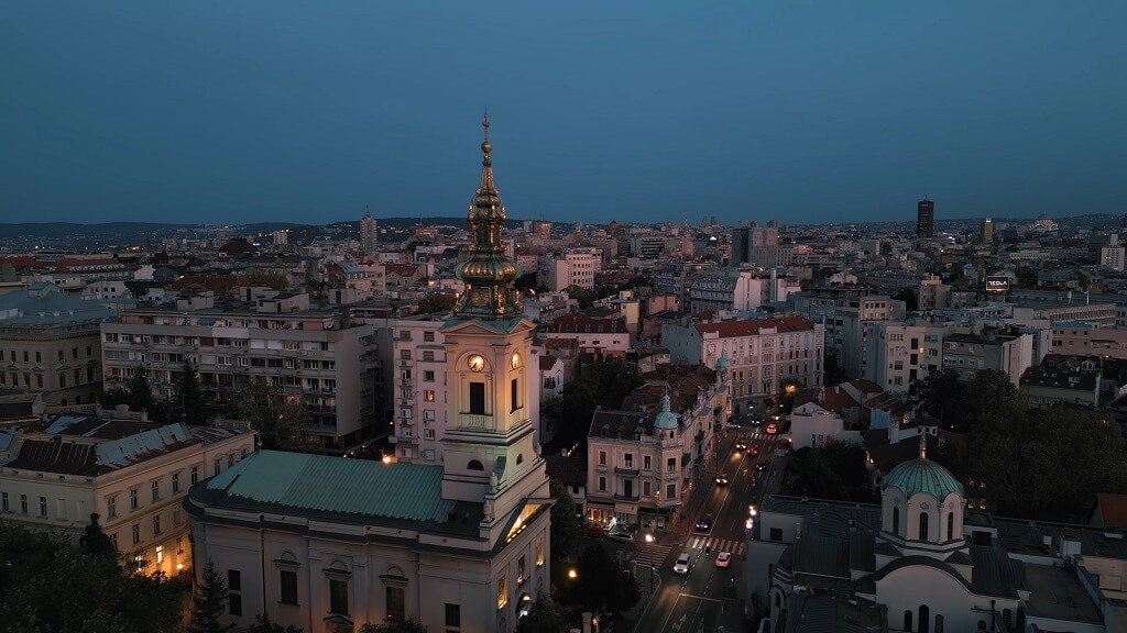 Evening aerial view of Belgrade, Serbia, featuring the illuminated Cathedral Church of St. Michael and surrounding city buildings