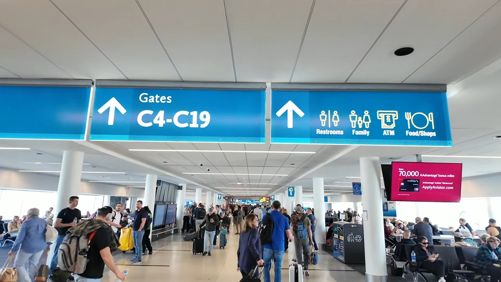 Terminal concourse at Charlotte Douglas International Airport with overhead gate signage and passengers moving toward departure gates