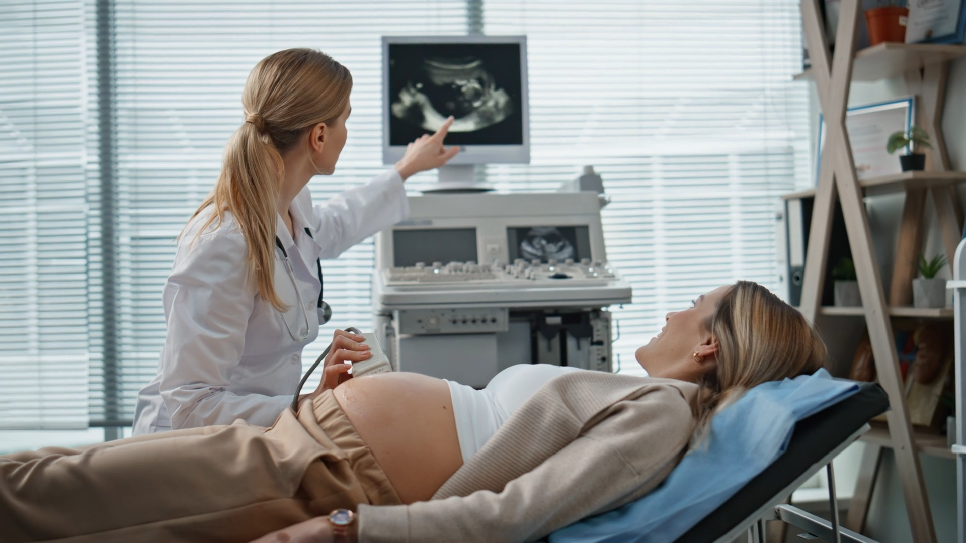 A pregnant woman lies on an examination bed while a doctor performs an ultrasound and discusses the findings on the monitor