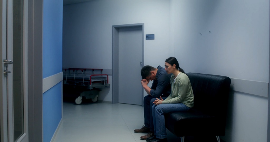 Patients seated in a hospital waiting area near an emergency department hallway, limited inpatient access context