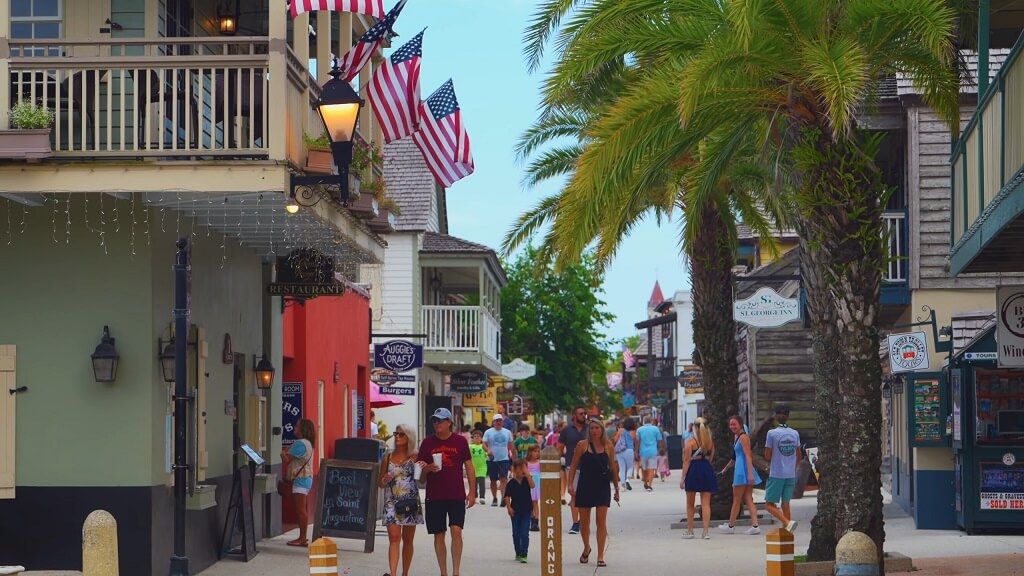 Busy historic street in downtown St. Augustine with pedestrians, colorful storefronts, and palm trees lining the walkway
