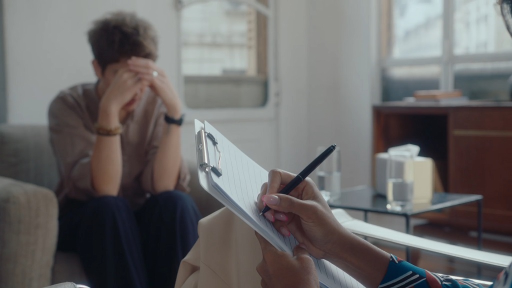 Clinical consultation setting with paperwork in focus and a patient seated in the background, mental health assessment environment