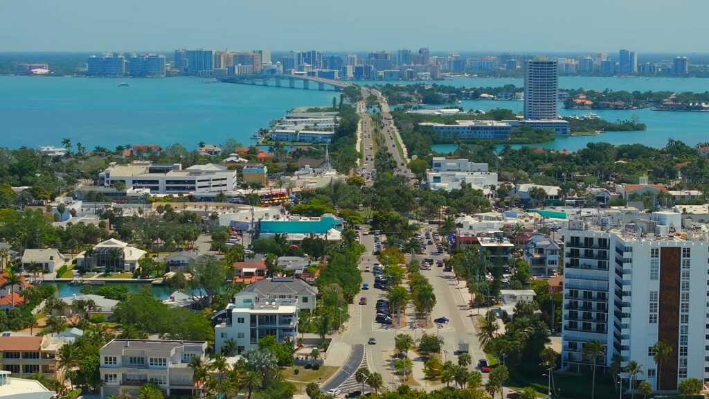Aerial view of a coastal city with waterways, bridges, and high-rise buildings near turquoise blue ocean water