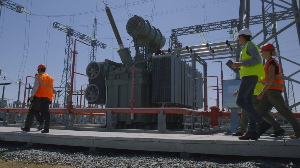 Engineers walking past a high-voltage transformer installation at an outdoor power substation