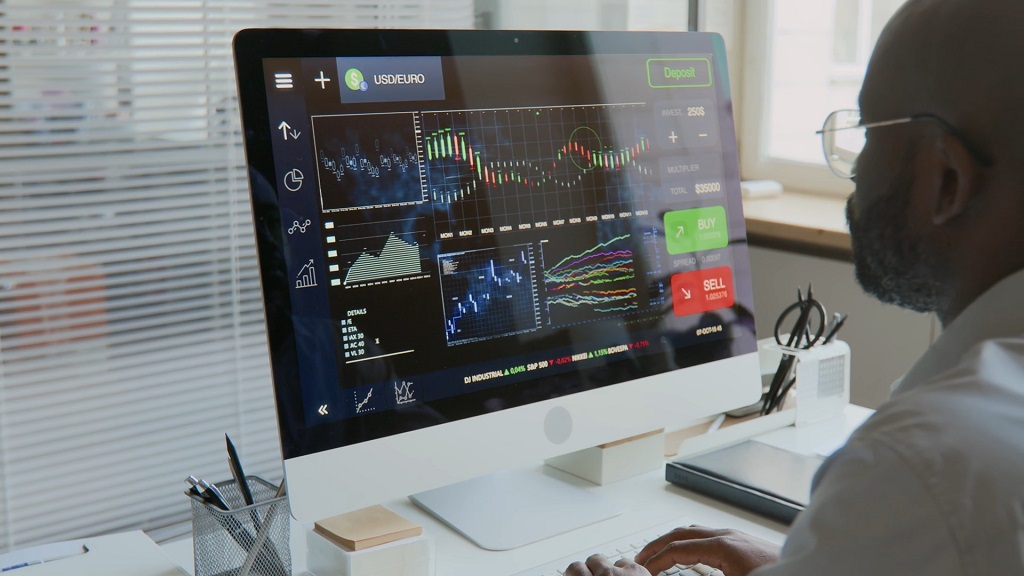 Man analyzing market charts and trading dashboard on a desktop computer, reviewing stock and currency data