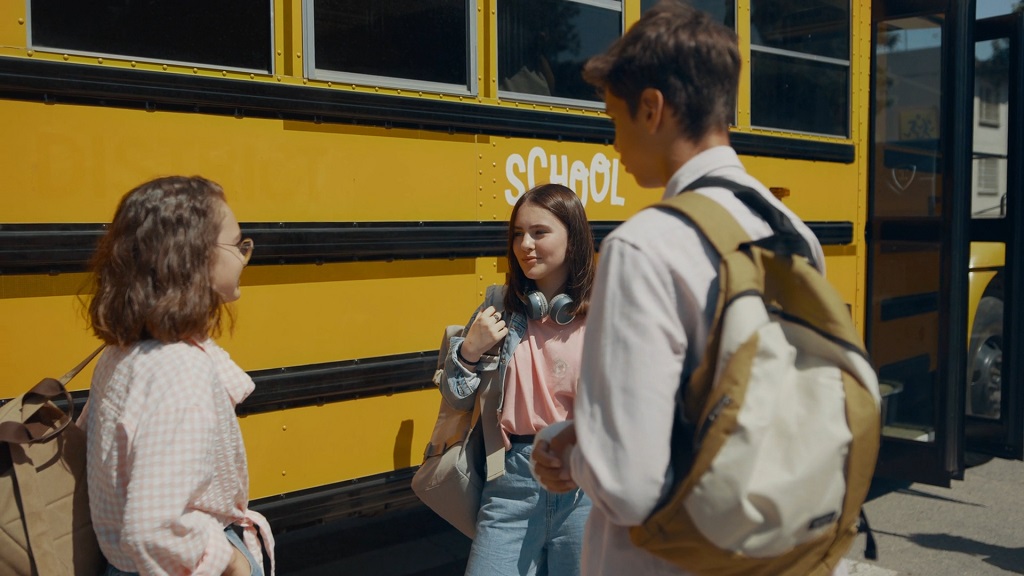 High school students standing beside a yellow school bus after classes