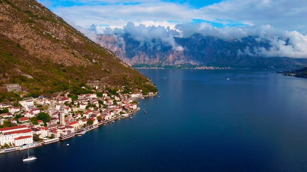 Coastal view of Kotor Bay in Montenegro, with a historic seaside town along the shoreline and mountains rising behind the water