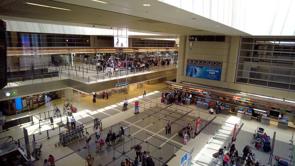Wide interior view of Los Angeles International Airport showing passenger check-in counters, queue barriers, and travelers moving through the terminal during daytime