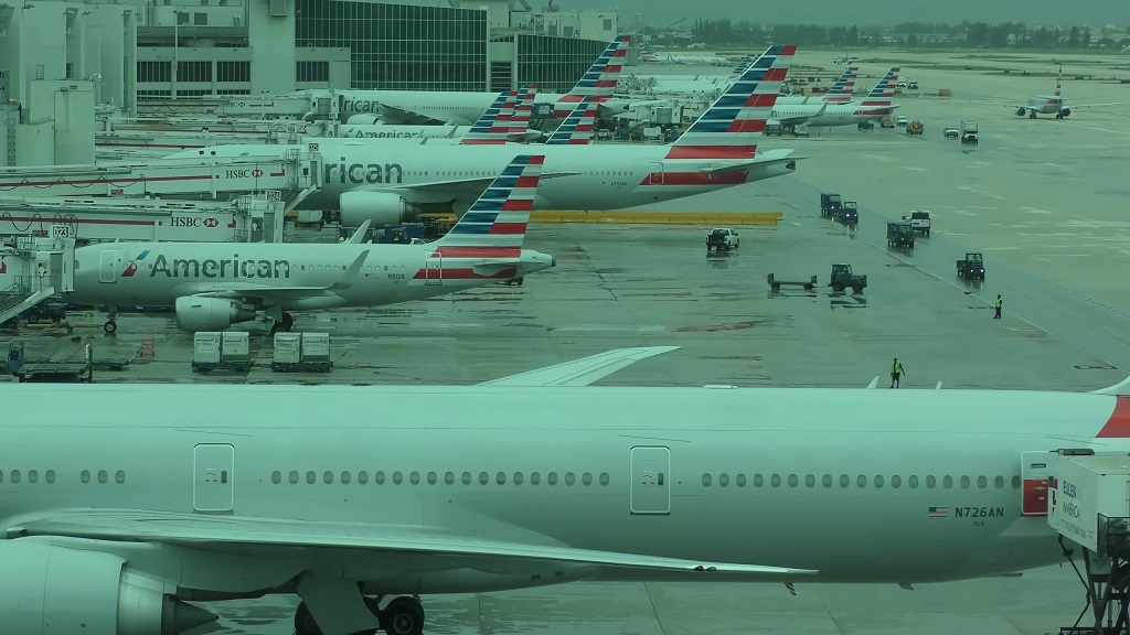 American Airlines aircraft parked at gates at Miami International Airport during rainy conditions, with ground service vehicles visible