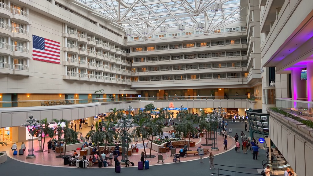 Large terminal atrium at Orlando International Airport featuring indoor palm trees, seating areas, and travelers inside the concourse