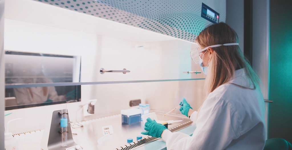 Laboratory technician working under a sterile hood, preparing samples for pharmaceutical or biomanufacturing processes