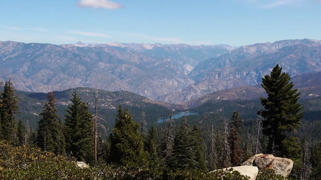 Expansive mountain view along the Kings Canyon Scenic Byway, with forested ridges, layered Sierra Nevada peaks, and a distant alpine lake below