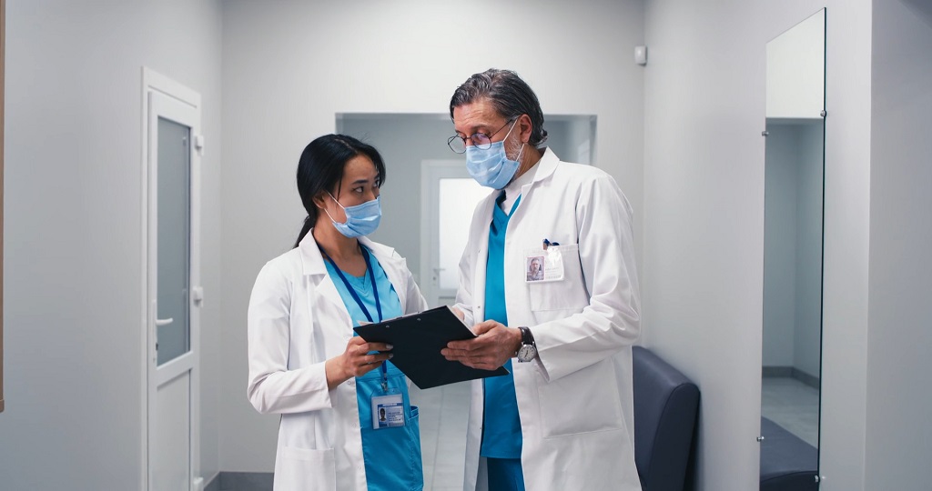 Two medical professionals in a clinical hallway reviewing patient records together, illustrating coordinated care and decision-making within modern healthcare systems