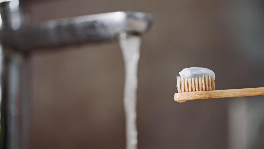 Tap water flowing from a faucet next to a toothbrush with toothpaste, illustrating the role of water in daily oral hygie
