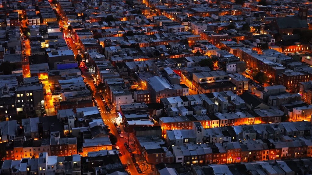 Aerial nighttime view of a dense Pennsylvania city neighborhood with rows of residential buildings and illuminated streets, showing compact urban housing patterns