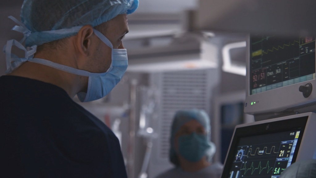 Medical staff in surgical masks observe vital sign monitors during a hospital procedure, ensuring patient stability