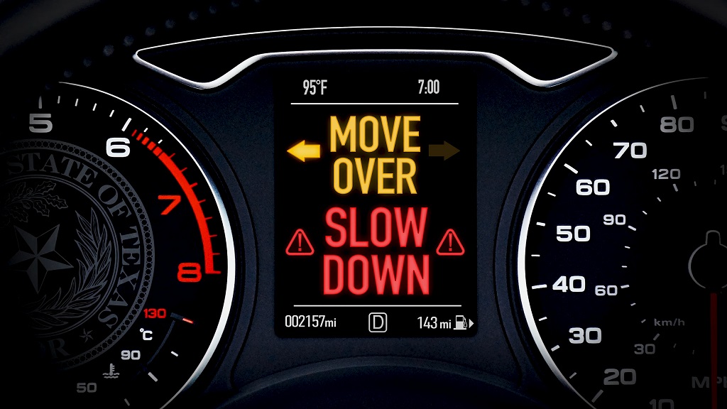 Digital vehicle dashboard display showing a safety warning that reads “Move Over Slow Down,” reinforcing the driver’s legal responsibility to adjust speed or lane position near roadside workers