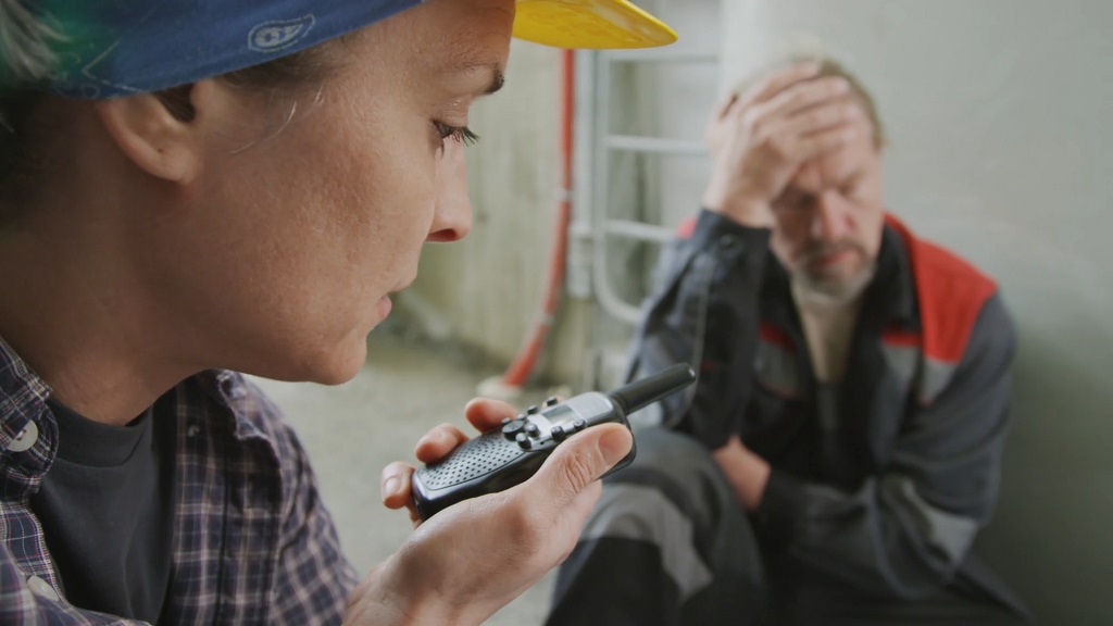 Worker using a radio to report an accident while an injured coworker sits in pain at the job site