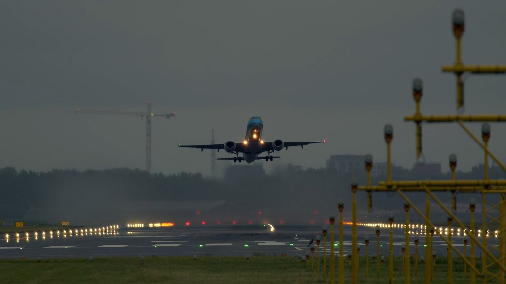 Commercial aircraft taking off from a runway at dusk, with illuminated runway lights and airport approach lighting visible
