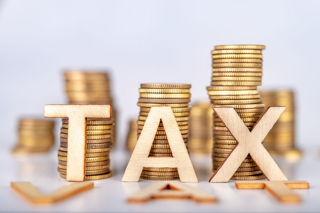 Bars stacked from coins on a white table. TAX and Tax letters with wooden letters based on coins. White background.